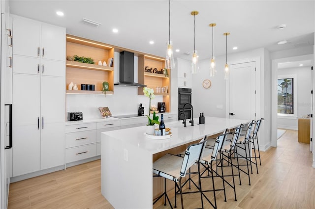 103 4th St N Unit A, Bradenton Beach, FL 34217 - kitchen featuring wall chimney exhaust hood, open shelves, an island with sink, light wood-style floors, and black appliances