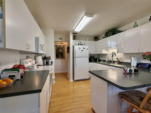 3828 6th Ave W, Palmetto, FL 34221 - kitchen featuring white appliances, a peninsula, dark countertops, light wood-style floors, and a kitchen breakfast bar