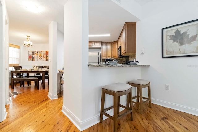 5401 Bentgrass Dr Unit 1-113, Sarasota, FL 34235 - kitchen with freestanding refrigerator, light wood-style floors, a kitchen bar, a chandelier, and baseboards