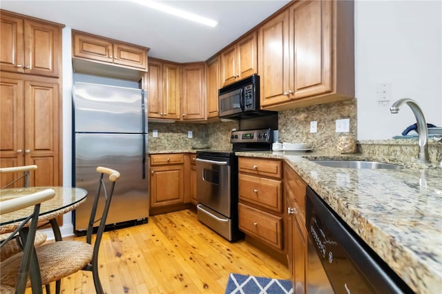 5401 Bentgrass Dr Unit 1-113, Sarasota, FL 34235 - kitchen with black appliances, a sink, light wood-style flooring, brown cabinets, and light stone countertops