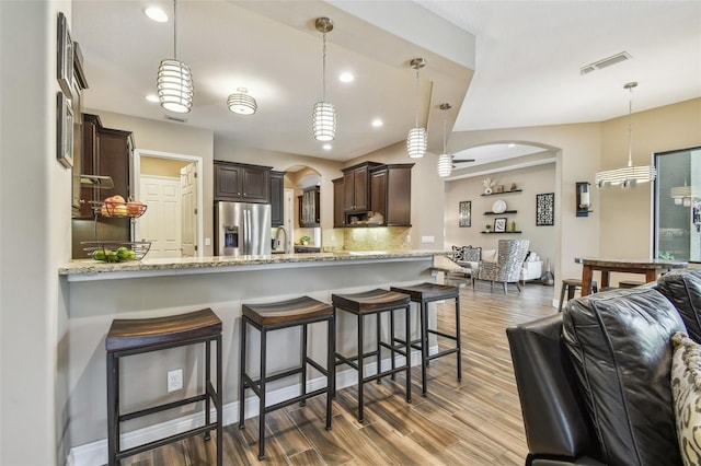 16246 26th St E, Parrish, FL 34219 - kitchen featuring stainless steel fridge, arched walkways, dark brown cabinetry, light stone countertops, and decorative light fixtures