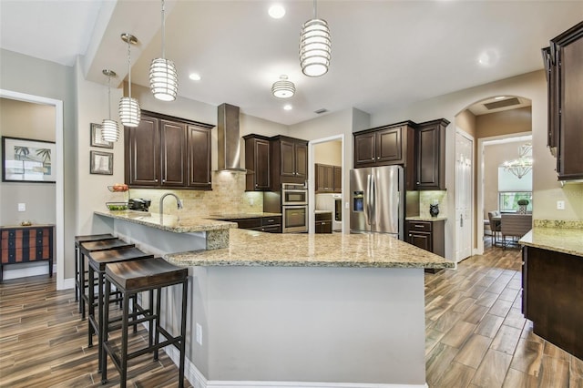 16246 26th St E, Parrish, FL 34219 - kitchen featuring stainless steel appliances, wall chimney range hood, dark brown cabinetry, a peninsula, and light wood finished floors
