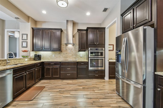 16246 26th St E, Parrish, FL 34219 - kitchen featuring appliances with stainless steel finishes, a sink, wall chimney exhaust hood, dark brown cabinetry, and light wood-style flooring