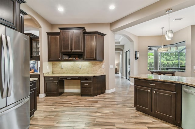 16246 26th St E, Parrish, FL 34219 - kitchen featuring appliances with stainless steel finishes, arched walkways, dark brown cabinets, decorative backsplash, and light stone counters
