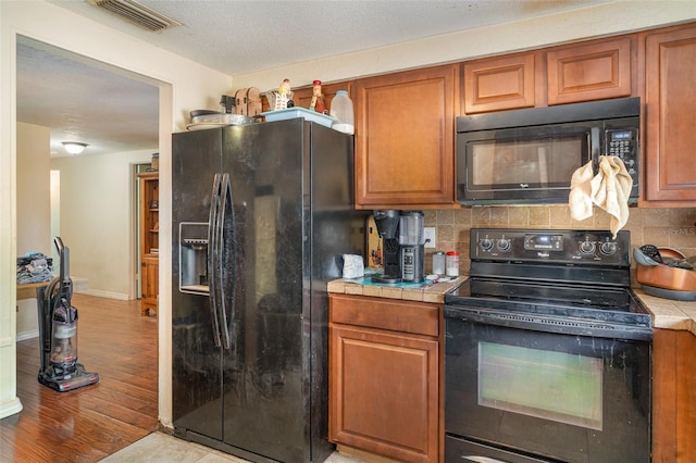 3921 Marlborough Pl, Sarasota, FL 34241 - kitchen featuring black appliances, tile countertops, tasteful backsplash, and brown cabinetry