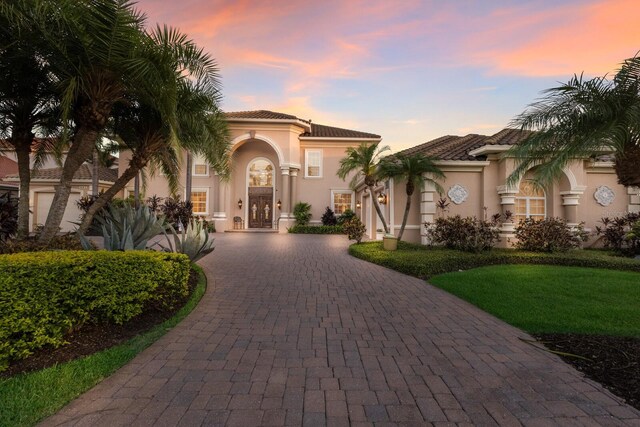 801 3rd St E, Palmetto, FL 34221 - mediterranean / spanish-style house featuring curved driveway, stucco siding, a tile roof, french doors, and a yard