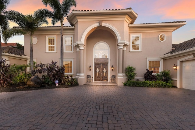 801 3rd St E, Palmetto, FL 34221 - exterior entry at dusk featuring french doors, decorative driveway, stucco siding, and a tile roof