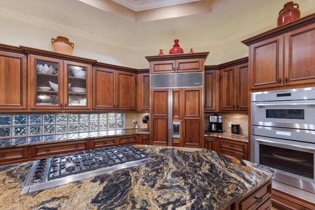 801 3rd St E, Palmetto, FL 34221 - kitchen featuring appliances with stainless steel finishes, decorative backsplash, a tray ceiling, dark stone countertops, and ornamental molding