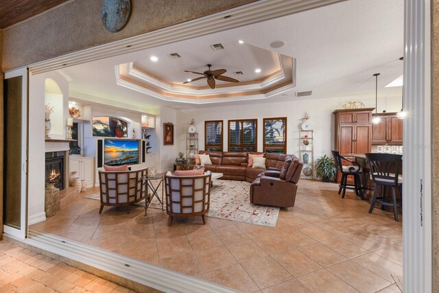 801 3rd St E, Palmetto, FL 34221 - living room featuring a raised ceiling, ornamental molding, a ceiling fan, a fireplace, and light tile patterned flooring