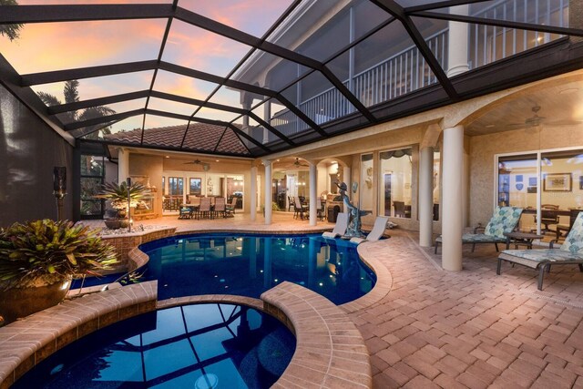 801 3rd St E, Palmetto, FL 34221 - pool at dusk with a ceiling fan, outdoor dining space, a patio area, a pool with connected hot tub, and glass enclosure