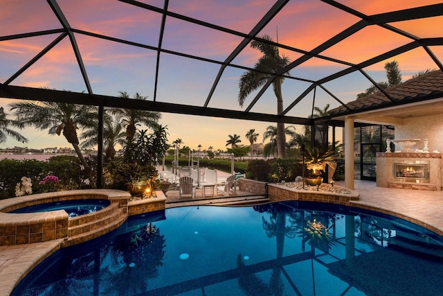 801 3rd St E, Palmetto, FL 34221 - pool at dusk featuring a patio, glass enclosure, a warm lit fireplace, and a pool with connected hot tub