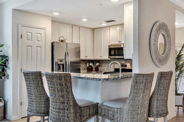 5843 Wake Forest Run Unit 104, Bradenton, FL 34211 - kitchen with appliances with stainless steel finishes, dark stone counters, backsplash, a peninsula, and baseboards