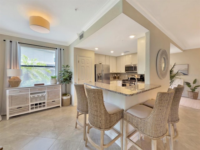 5843 Wake Forest Run Unit 104, Bradenton, FL 34211 - kitchen with stainless steel appliances, light stone countertops, a kitchen breakfast bar, tasteful backsplash, and ornamental molding
