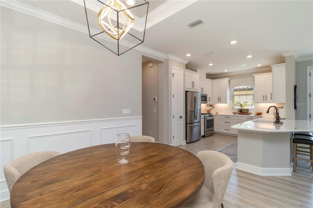 15752 Sacile Ln, Bradenton, FL 34211 - dining space featuring crown molding, light wood-style flooring, a chandelier, wainscoting, and a decorative wall