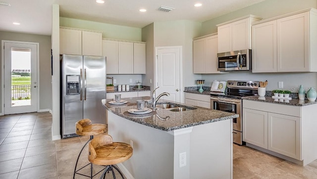 5116 Rosado Run, Lakewood Ranch, FL 34211 - kitchen with stainless steel appliances, a sink, dark stone counters, a center island with sink, and recessed lighting