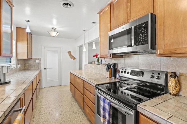 1324 Augusta Ln S, Saint Petersburg, FL 33707 - kitchen with appliances with stainless steel finishes, decorative backsplash, decorative light fixtures, dark speckled floor, and tile counters
