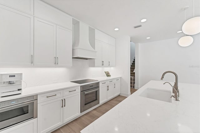8069 Tidal Pointe Way, Sarasota, FL 34240 - kitchen featuring oven, a sink, custom range hood, light wood finished floors, and white cabinets
