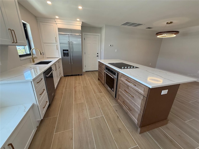 808 25th Ave W, Palmetto, FL 34221 - kitchen with appliances with stainless steel finishes, a sink, light wood-style floors, a kitchen island, and light stone countertops