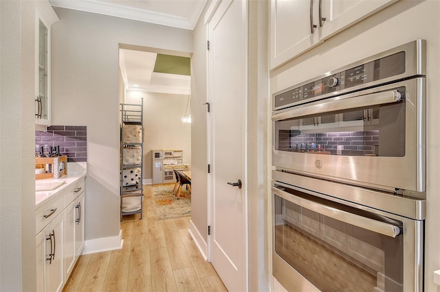1919 Woodleaf Hammock Ct, Bradenton, FL 34211 - kitchen with crown molding, double oven, white cabinetry, light wood-style floors, and tasteful backsplash