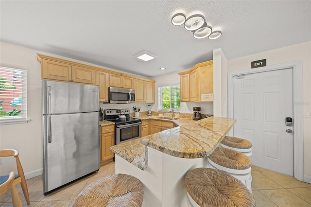 308 Canal Rd, Sarasota, FL 34242 - kitchen featuring appliances with stainless steel finishes, light brown cabinetry, a sink, a peninsula, and a kitchen breakfast bar