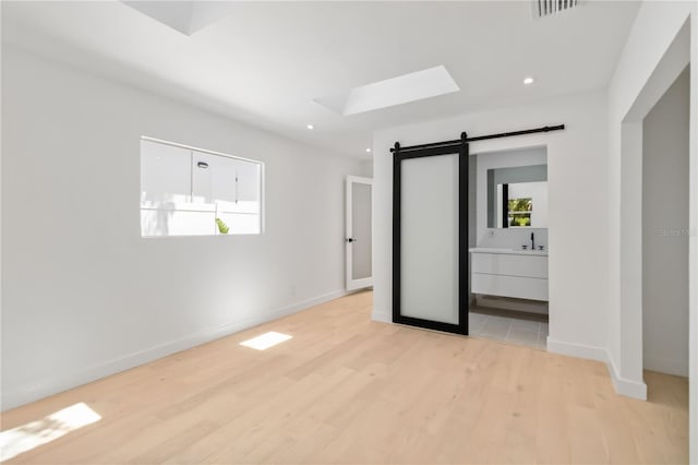 2410 Floyd St, Sarasota, FL 34239 - unfurnished bedroom with a barn door, light wood-type flooring, multiple windows, a skylight, and recessed lighting