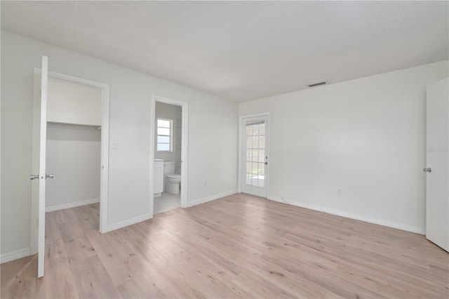 478 Orange Dr NW, Port Charlotte, FL 33952 - unfurnished bedroom featuring light wood-type flooring, a walk in closet, baseboards, and ensuite bath
