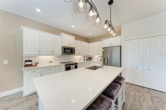 1219 Thornbury Dr, Parrish, FL 34219 - kitchen featuring appliances with stainless steel finishes, a sink, light wood-style floors, white cabinetry, and a center island with sink