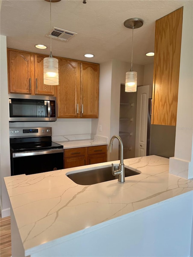 4037 Crockers Lake Blvd Unit 24, Sarasota, FL 34238 - kitchen featuring appliances with stainless steel finishes, light stone counters, a sink, brown cabinetry, and hanging light fixtures