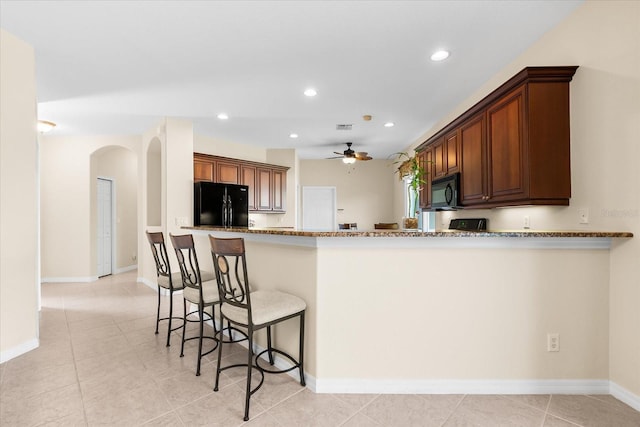 138 Tiziano Way N, Venice, FL 34275 - kitchen with black appliances, arched walkways, a ceiling fan, a breakfast bar area, and stone countertops