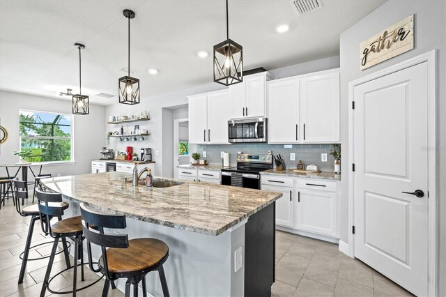 17547 Cantarina Cv, Bradenton, FL 34211 - kitchen featuring appliances with stainless steel finishes, a sink, decorative backsplash, open shelves, and light stone counters