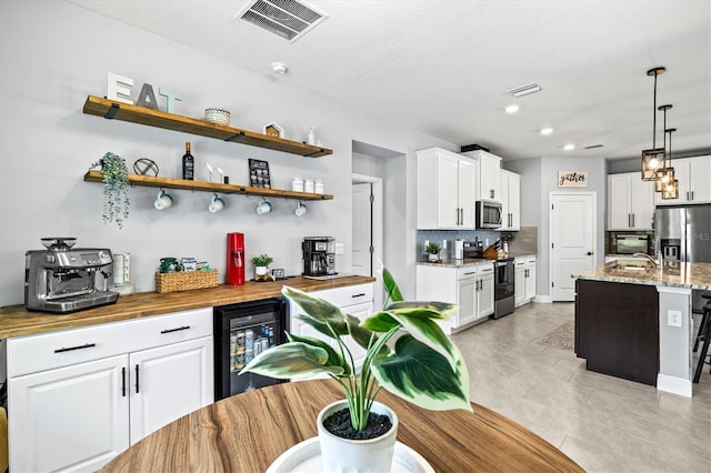 17547 Cantarina Cv, Bradenton, FL 34211 - kitchen featuring stainless steel appliances, wine cooler, white cabinetry, tasteful backsplash, and light stone counters