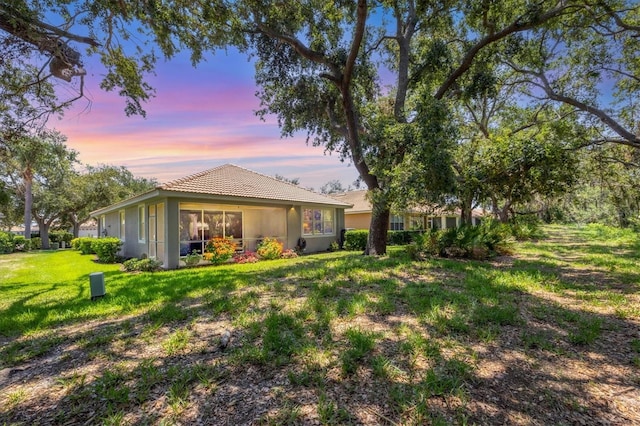 4121 Reflections Pkwy, Sarasota, FL 34233 - back of house at dusk with stucco siding, a lawn, and a tile roof