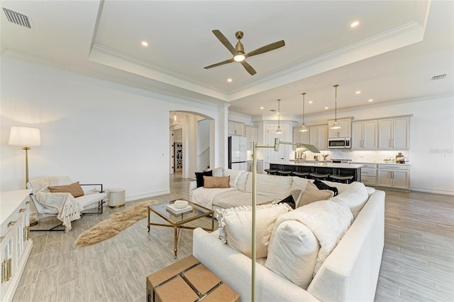 501 Maraviya Blvd, Nokomis, FL 34275 - living area featuring arched walkways, a ceiling fan, a raised ceiling, light wood-style flooring, and crown molding