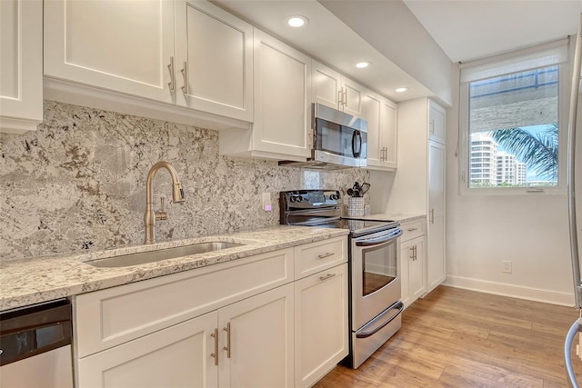 1115 Gulf Of Mexico Dr Unit 304, Longboat Key, FL 34228 - kitchen with stainless steel appliances, a sink, white cabinets, light wood finished floors, and tasteful backsplash