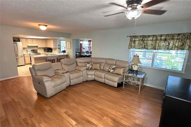 1111 Harefield Cir, Sun City Center, FL 33573 - living room featuring a textured ceiling, a ceiling fan, light wood-type flooring, and baseboards