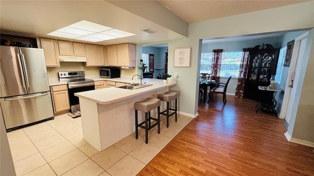 1111 Harefield Cir, Sun City Center, FL 33573 - kitchen with appliances with stainless steel finishes, under cabinet range hood, a sink, light wood-style floors, and a breakfast bar area