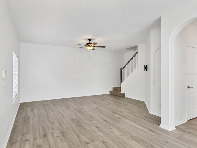262 Cape Harbour Loop Unit 101, Bradenton, FL 34212 - unfurnished living room with arched walkways, a ceiling fan, light wood-style flooring, stairs, and baseboards