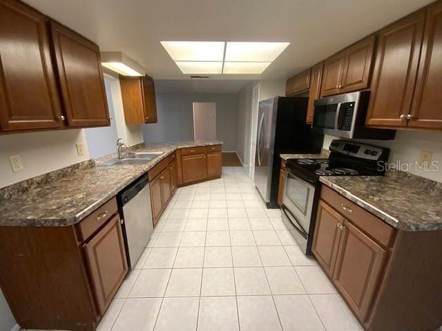 6923 13th Ave E, Bradenton, FL 34208 - kitchen with stainless steel appliances, a sink, light tile patterned floors, a peninsula, and brown cabinetry