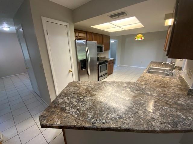 6923 13th Ave E, Bradenton, FL 34208 - kitchen with appliances with stainless steel finishes, a sink, light tile patterned floors, brown cabinetry, and a peninsula