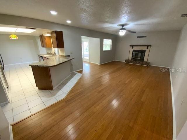6923 13th Ave E, Bradenton, FL 34208 - kitchen featuring ceiling fan, a sink, a glass covered fireplace, a peninsula, and light wood-style floors