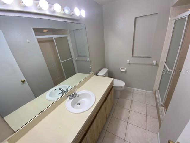 6923 13th Ave E, Bradenton, FL 34208 - bathroom featuring a stall shower, toilet, vanity, tile patterned flooring, and baseboards