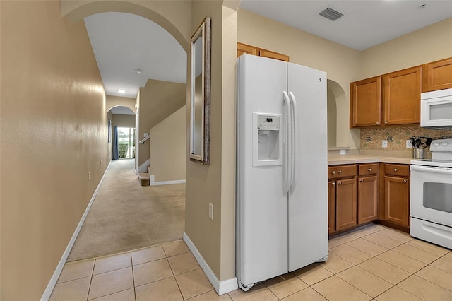 3707 45th Ter W Unit 104, Bradenton, FL 34210 - kitchen with white appliances, arched walkways, brown cabinetry, light countertops, and light tile patterned flooring