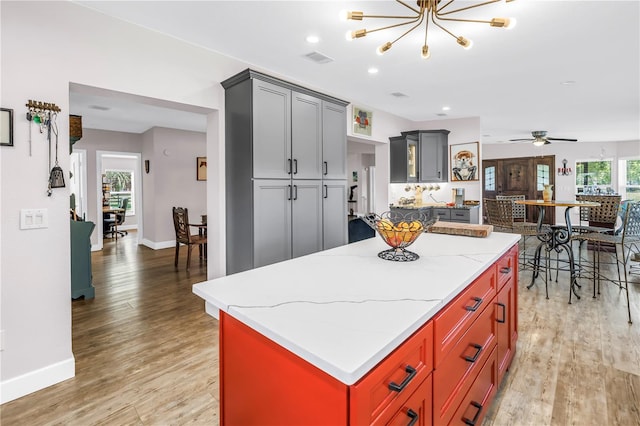 12714 Tyler Run Ave, Odessa, FL 33556 - kitchen featuring light wood-style flooring, baseboards, a chandelier, a center island, and light stone countertops