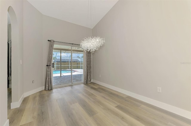 5742 39th Street Cir E, Bradenton, FL 34203 - unfurnished room with arched walkways, baseboards, light wood finished floors, high vaulted ceiling, and a chandelier