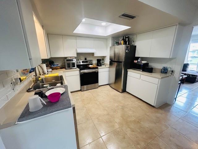 8409 43rd Ave W, Bradenton, FL 34209 - kitchen featuring appliances with stainless steel finishes, under cabinet range hood, a raised ceiling, a sink, and white cabinetry