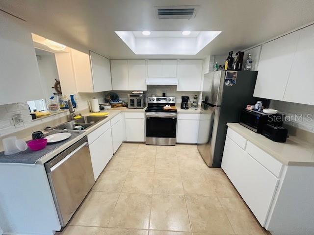 8409 43rd Ave W, Bradenton, FL 34209 - kitchen featuring stainless steel appliances, under cabinet range hood, a raised ceiling, a sink, and light tile patterned flooring