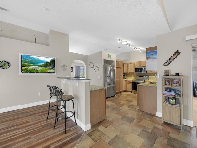 27 Sea Shark Path, Palm Coast, FL 32164 - kitchen featuring appliances with stainless steel finishes, lofted ceiling, a kitchen breakfast bar, tasteful backsplash, and light stone counters