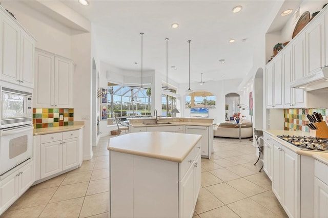 7214 Marlow Pl, University Park, FL 34201 - kitchen with white appliances, a kitchen island with sink, arched walkways, open floor plan, and decorative backsplash