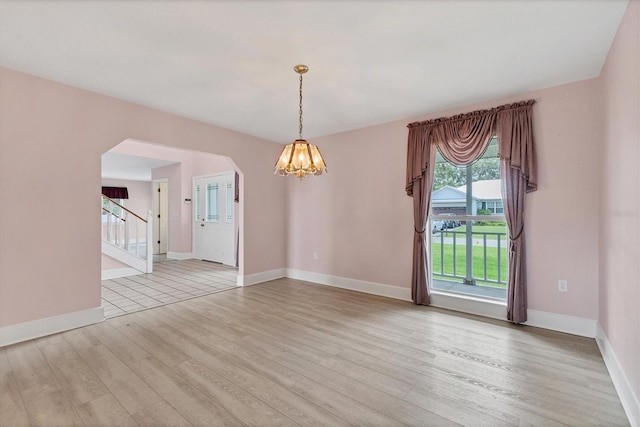 2002 8th St W, Palmetto, FL 34221 - spare room with light wood finished floors, a chandelier, arched walkways, stairway, and baseboards