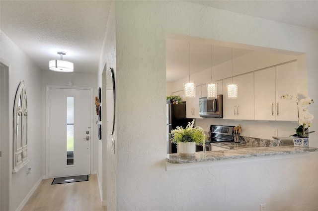 6024 28th St W, Bradenton, FL 34207 - kitchen featuring stainless steel appliances, a textured wall, light wood-style floors, a textured ceiling, and decorative light fixtures